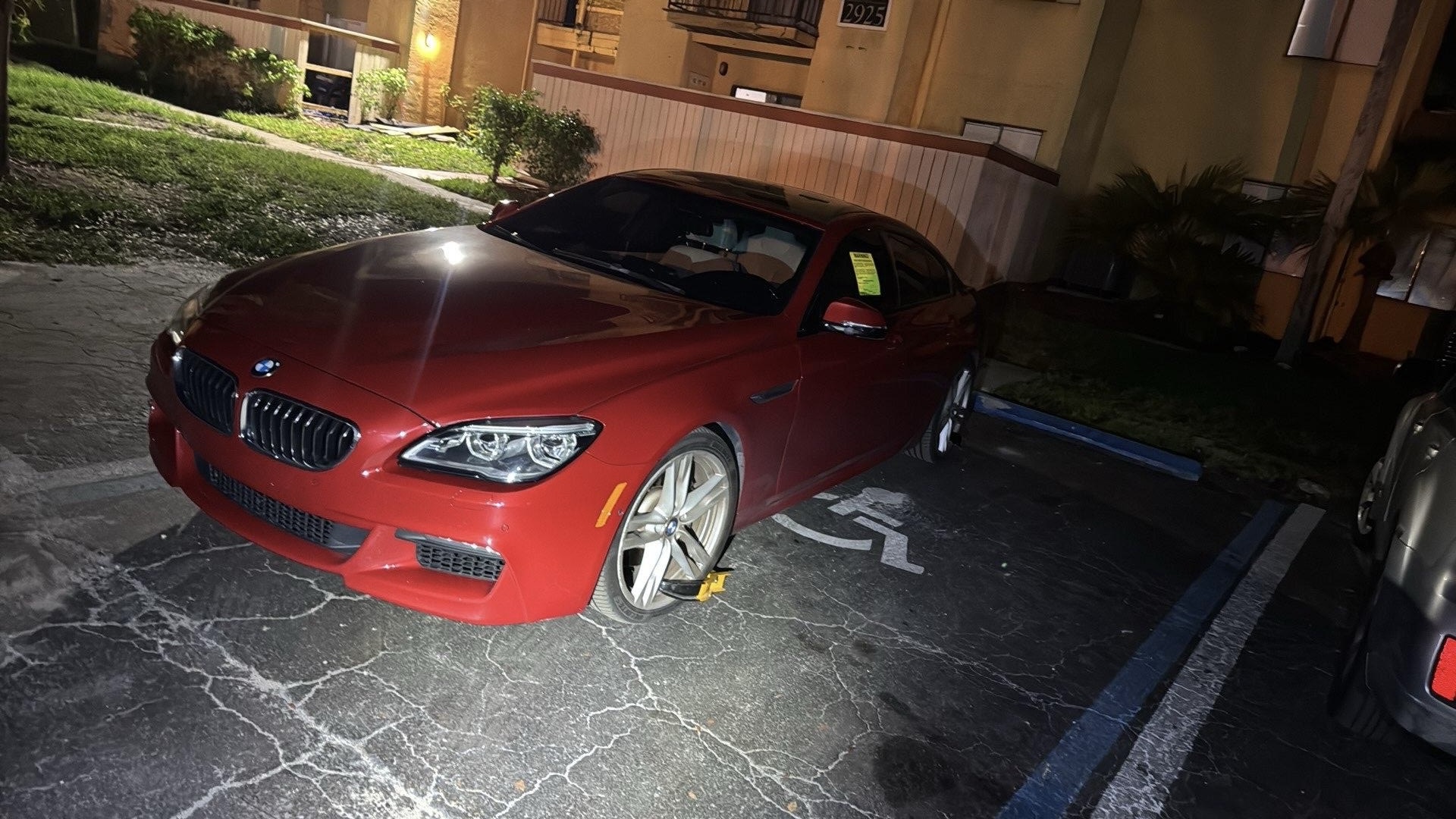 Red vehicle immobilized with wheel lock in parking space